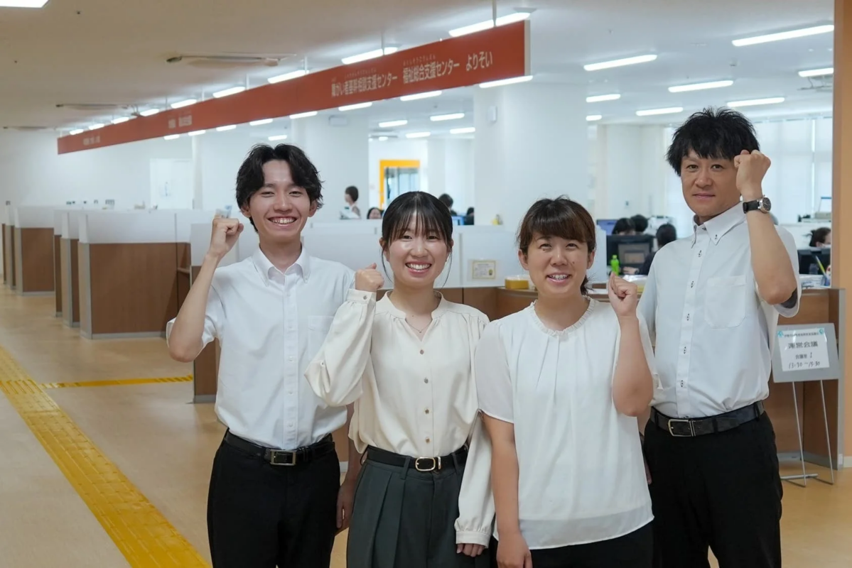 オフィスで働く4人の男女が、笑顔で拳を突き上げてポーズをとっています。