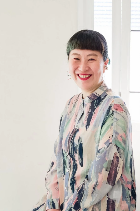 カラフルな抽象柄のシャツを着たアジア人女性が、カメラに向かって満面の笑みを浮かべているポートレート