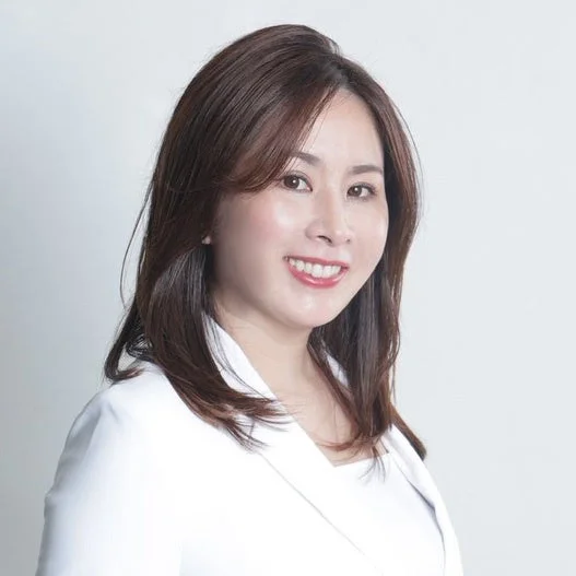 白い背景の前で、白いジャケットを着た笑顔のアジア人女性のポートレート。カメラをまっすぐ見ており、親しみやすくプロフェッショナルな印象を与えます。