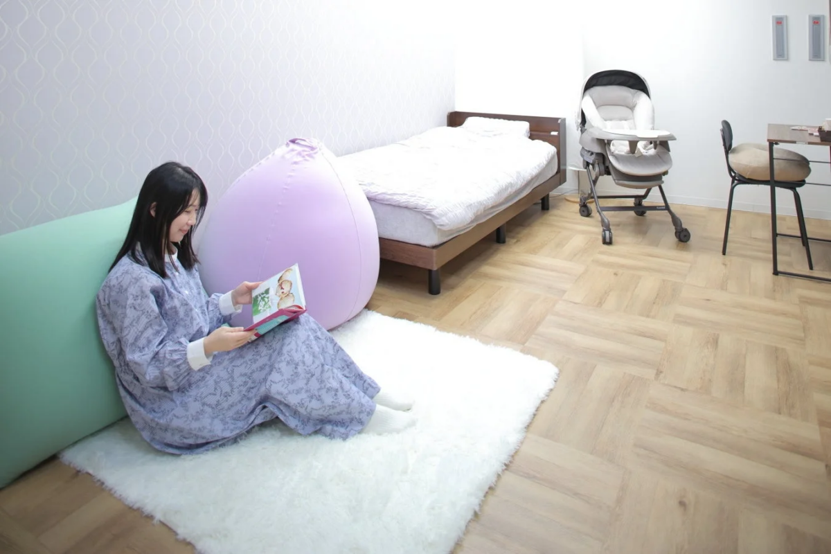 白いラグの上で女性が絵本を読んでくつろいでいる部屋の様子