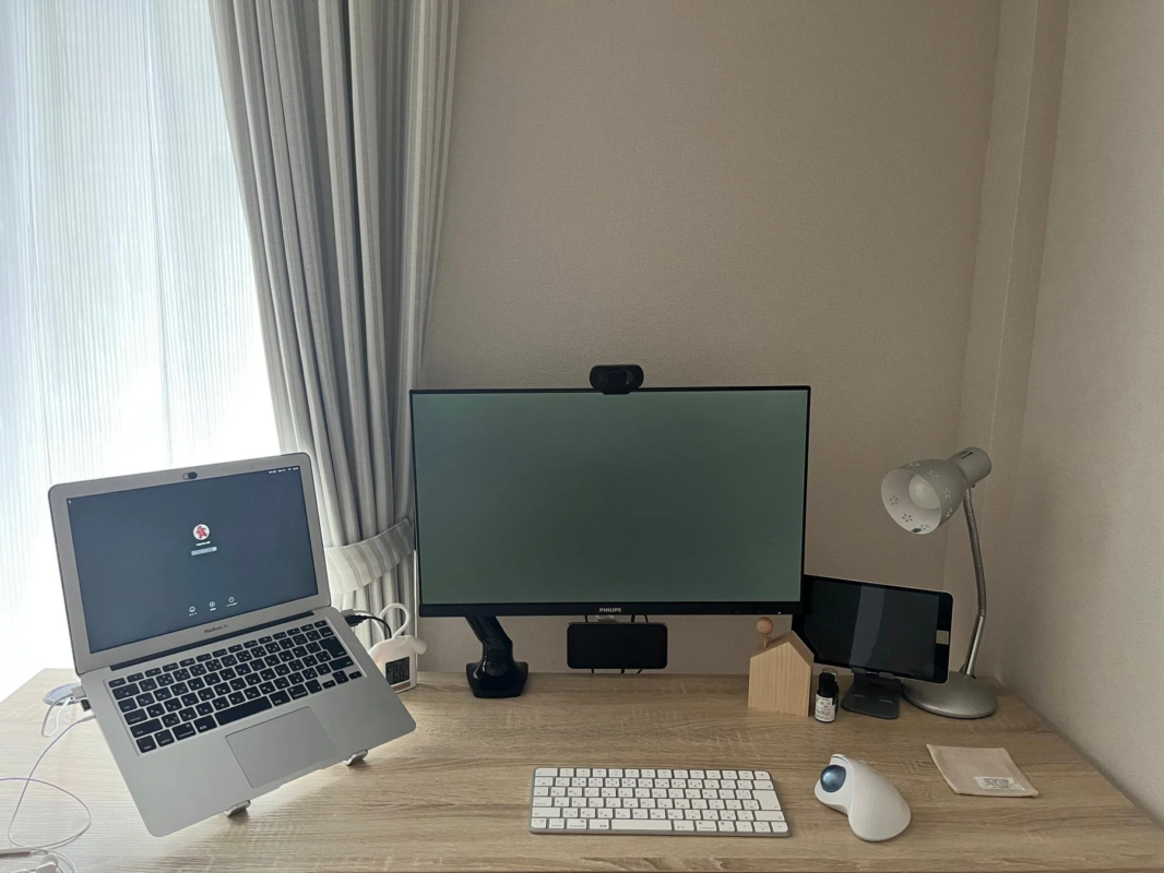 窓からの自然光が入る明るい部屋に設置された、MacBook Airと外部モニターを中心としたすっきりとしたホームオフィスのデスク環境