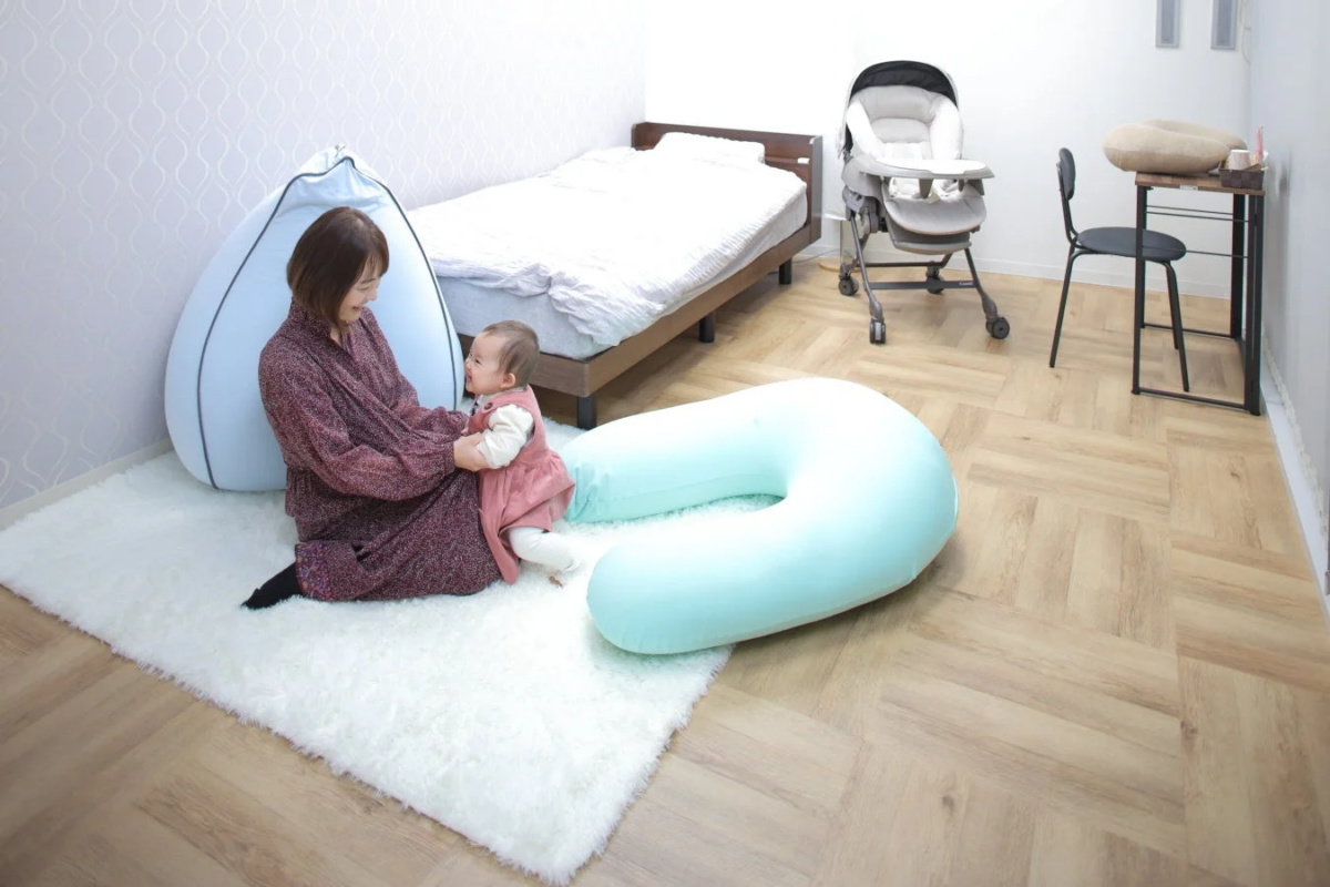 白いラグの上で女性が赤ちゃんを抱きかかえ、見つめ合っている様子
