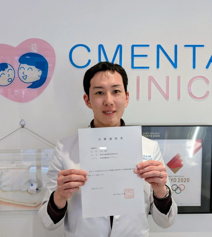 白衣姿で東京学芸大学大学院の合格通知書を掲げる久米康宏医師