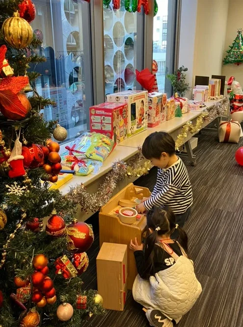クリスマスツリーやたくさんのプレゼントが飾られた室内で、2人の子供がおもちゃのキッチンセットで遊んでいます
