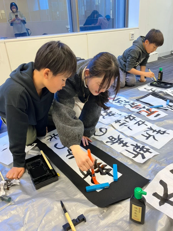 子供たちが床に座って書道に集中している様子