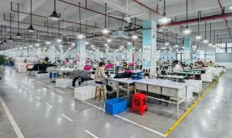 多数の労働者が個別の作業台でミシンなどの機械を使い、製品の製造に従事している大規模な工場内部の様子