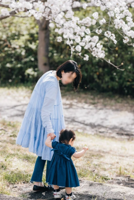 桜が咲く公園で、母親が小さな子供の手を引いて散歩している様子