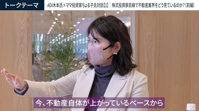 マスクを着用した女性が、不動産業界に関する対談でジェスチャーを交えながら話している様子。株式投資家の視点から不動産市場の動向について議論されており、特に不動産価格の上昇がテーマとなっている。