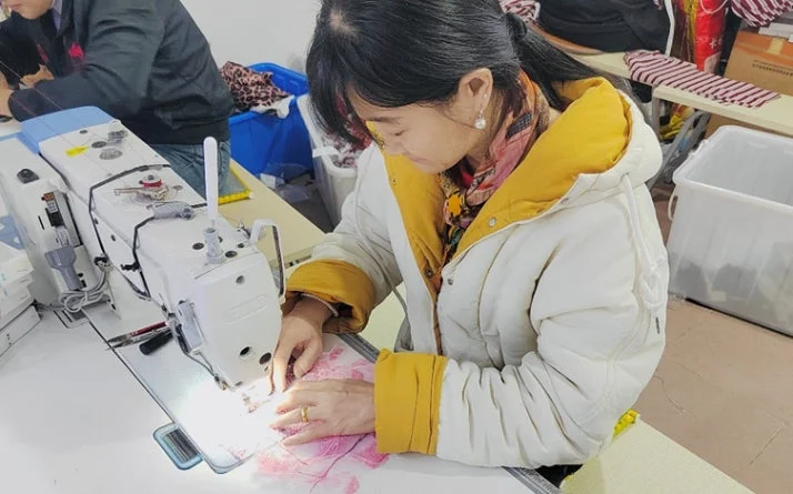 一人の女性が真剣な表情で工業用ミシンを操作し、布を縫い合わせている様子