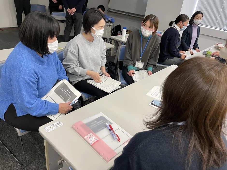 マスクを着用した複数人がテーブルを囲み、資料を見ながら会議や意見交換を行っている様子