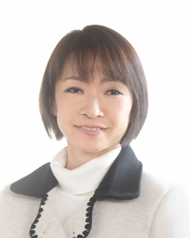 白い背景の前に立つ、白いタートルネックと黒い襟のコートを着用した女性のポートレート