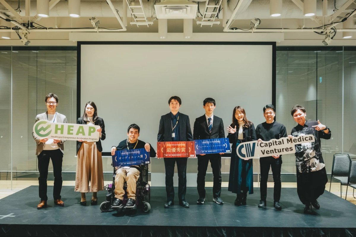 HEAP PITCH STAGE 2023の表彰式で、最優秀賞、オーディエンス賞、ヒューマンインパクト賞を受賞したヘルスケア分野の起業家たちが、プログラムロゴや受賞ボードを掲げてステージに並んでいる集合写真です。