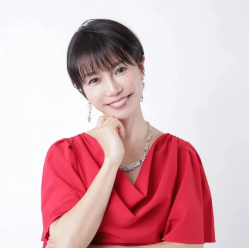 赤いトップスを着たショートヘアの女性が笑顔で顎に手を当てているポートレート