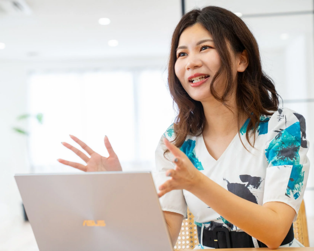 ノートパソコンの前に座った女性が笑顔で話している