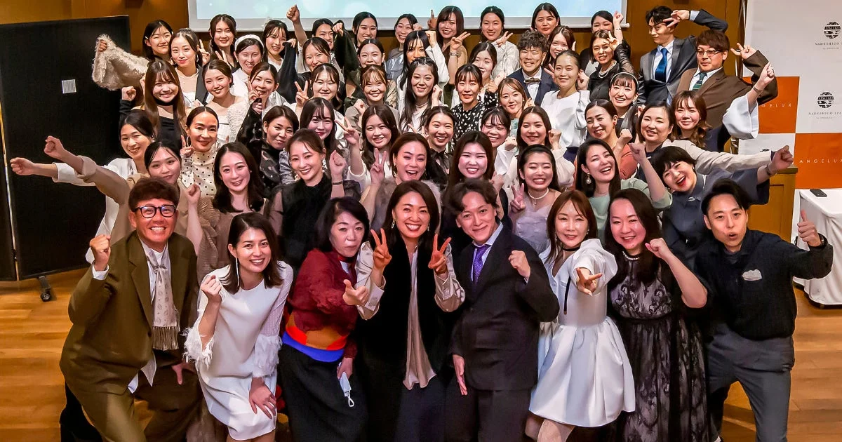 NADESHIKO SPA, ANGELUXのロゴが見える会場で、大勢の男女が笑顔でポーズを取る集合写真