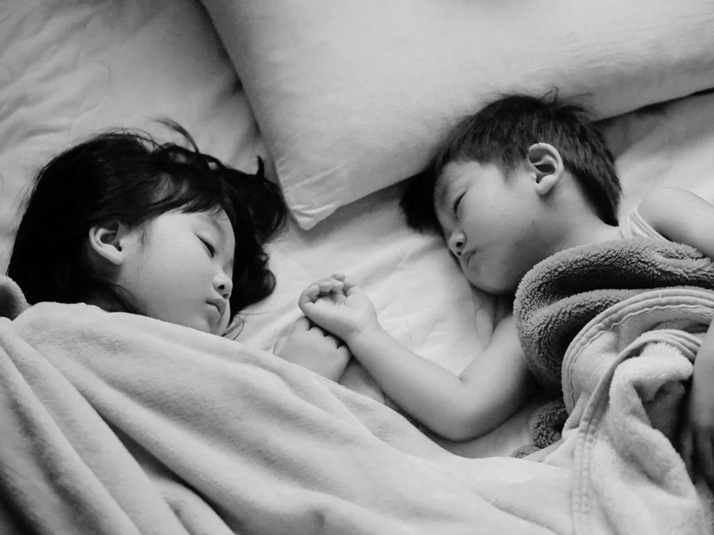 ベッドで手をつないで眠る二人の子供
